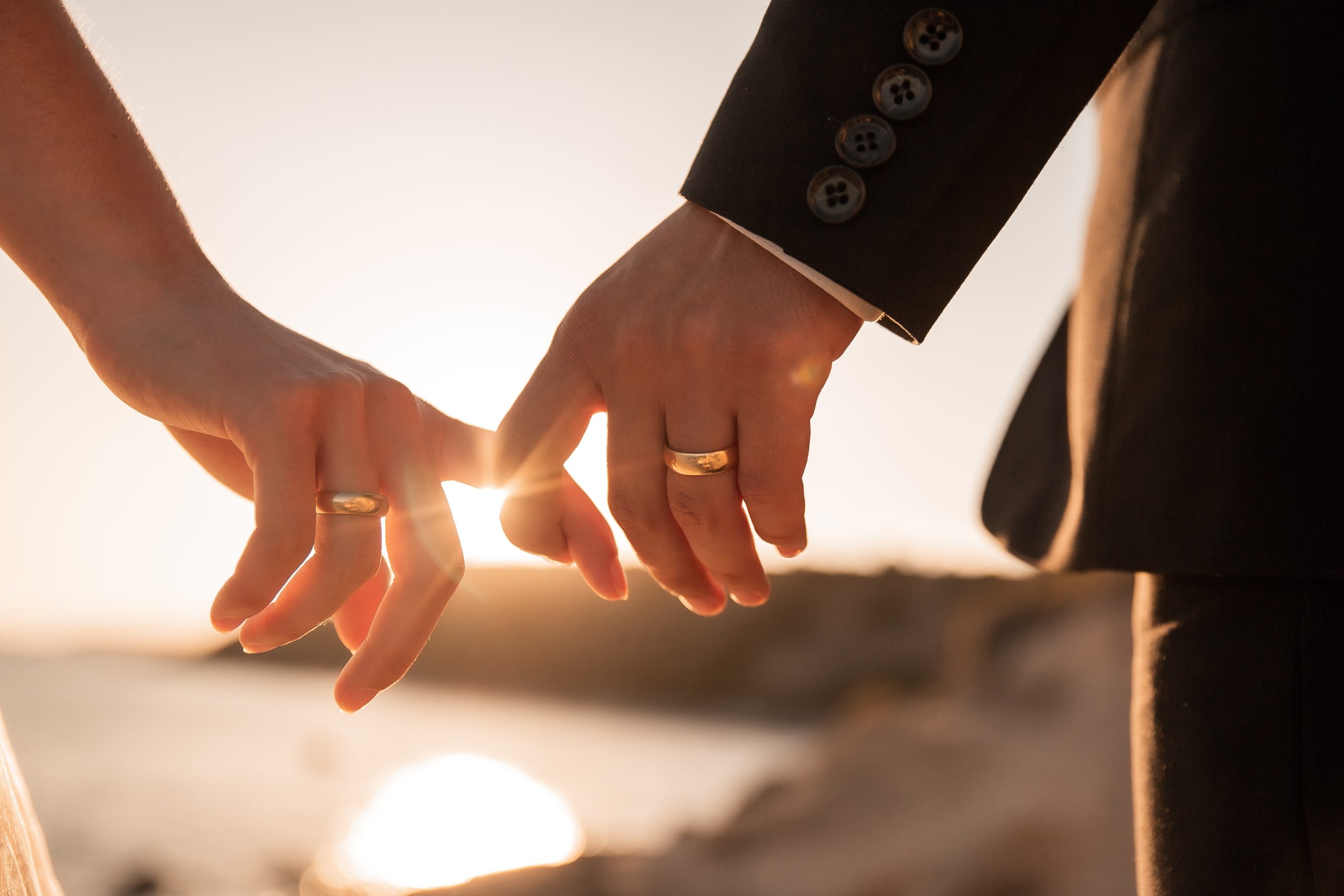 romantic couple holding hands fingers at sunset leaking wedding rings sunset rays bride groom wedding love couple golden hour .The article this image is on talks about How Marriage, Divorce, or Separation Can Affect Immigration Status