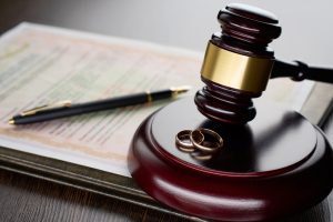 Divorce decree or marriage contract. Judge gavel with wedding rings and divorce decree. Marital agreement, legalities of divorce documents. The article this image is on talks about How Marriage, Divorce, or Separation Can Affect Immigration Status
